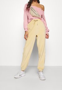Sweat-shirt rose à manches longues avec une épaule dénudée et des accents rayés, associé à un pantalon de jogging jaune clair et des baskets blanches.