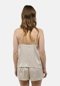 Ensemble de pyjama en satin beige clair comprenant un haut sans manches avec des bords festonnés et un short assorti, tous deux lisses et doux au toucher.