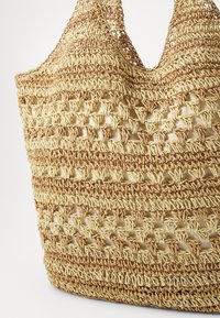 Woven straw bag with a textured design features a natural beige color, triangular cutouts, and dual shoulder straps for easy carrying.