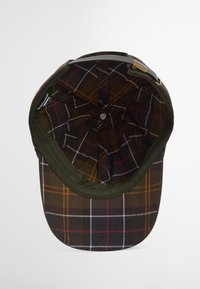 Boné verde escuro com um interior de xadrez apresentando padrões em castanho, branco e laranja; inclui um detalhe em metal e um botão no topo.