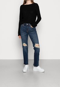 Maglione a maniche lunghe nero a costine abbinato a jeans blu stracciati con strappi sulle ginocchia, indossato con sneakers bianche con zeppa.