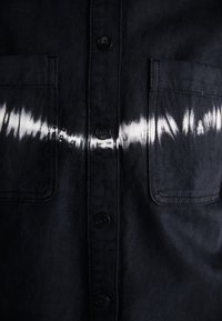 Cămașă din denim neagră cu un model alb de tie-dye pe piept, două buzunare frontale și nasturi negri pe placket.