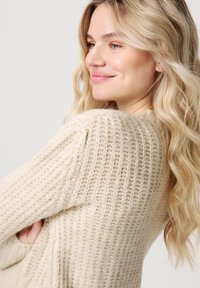 Sweter dzianinowy w kremowym kolorze o prążkowanej strukturze, z luźnym krojem i obniżonymi szwami na ramionach. Miękki i przytulny design.