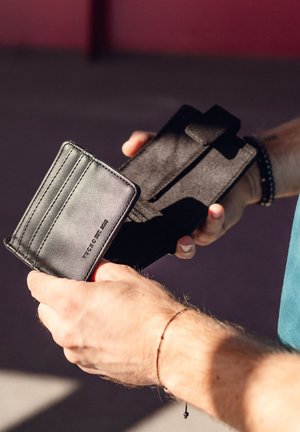 Black leather wallet with multiple card slots and a textured fabric exterior, held in one hand, displaying an organized design.
