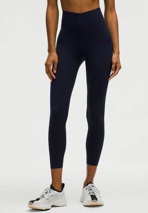 Hochtaillierte marineblaue Leggings aus dehnbarem Material mit glatter Textur und figurbetontem Design, kombiniert mit weißen Sportschuhen.