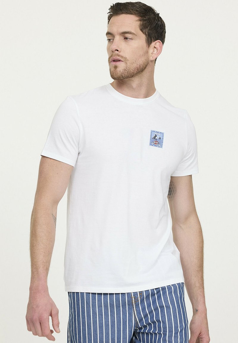 T-shirt en coton blanc à col rond et à manches courtes ; présente une petite patte nautique bleue sur le côté gauche de la poitrine.