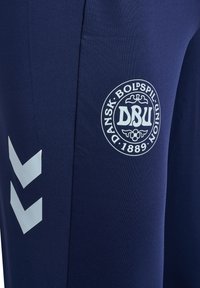 Marineblauer Sportstoff mit weißem Dansk Boldspil-Union (DBU) Logo und zwei weißen Chevron-Streifen auf der linken Seite.