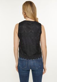 Svart, ärmlös virkade topp med texturerade mönster och scallop-kant, matchad med blå denim jeans.