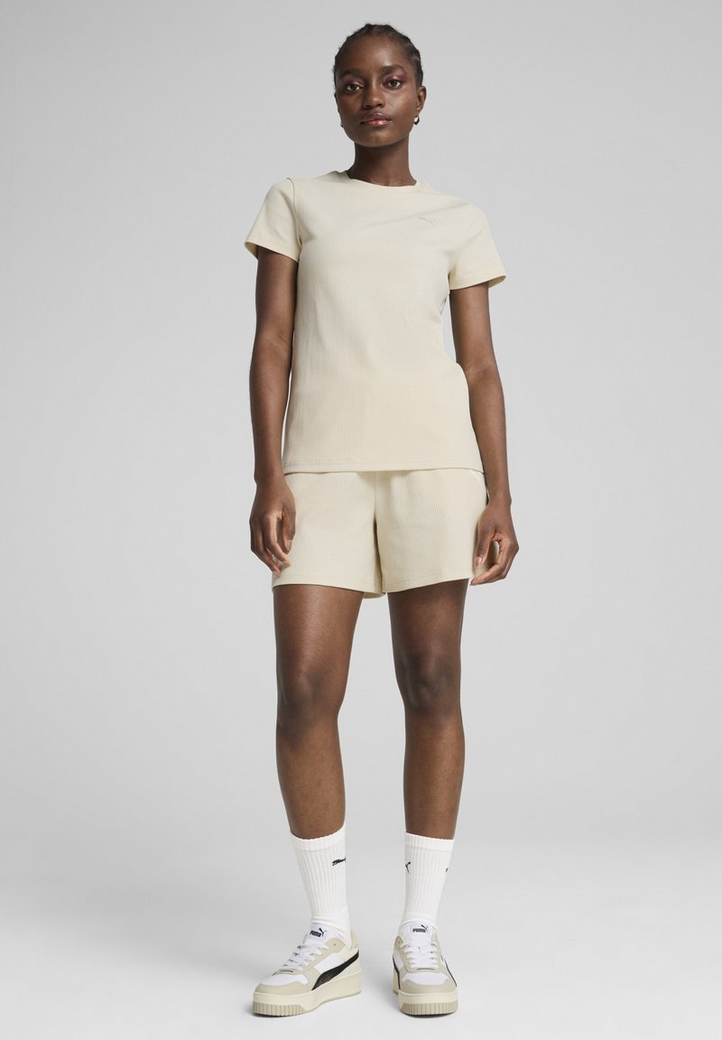 Lichtbeige geribbelde top met korte mouwen en bijpassende shorts. Draag met witte sokken en beige sneakers met zwarte accenten. Model staat rechtop.