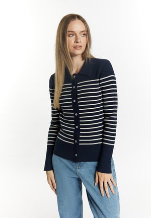 Navyblau gestreifter Cardigan mit vertikalen weißen Linien, gerippter Textur, Knopfriegel und Kragen; kombiniert mit hellblauen Jeans.