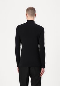 Top negro de manga larga con cuello simulado, diseño ajustado, textura suave y sin patrones o acentos visibles. Costuras planas, estilo minimalista.
