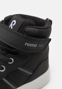 Sneaker alta nera con upper in tessuto, strisce grigie come accento, chiusura con lacci, suola in gomma e cinturino in velcro. Logo visibile sul cinturino.