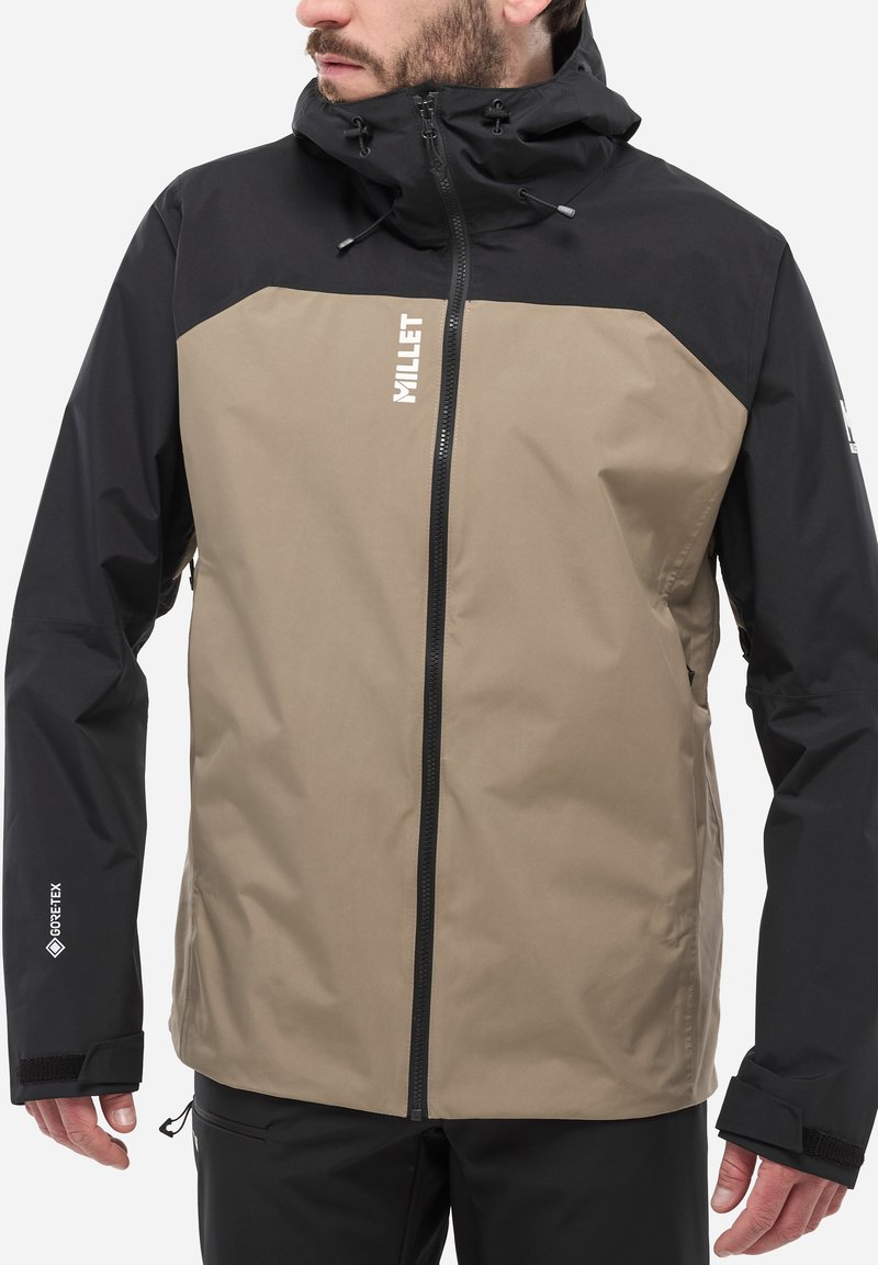 Veste pour homme avec un design en blocs de couleurs beige et noir. Fabriquée en matériau déperlant, avec une fermeture à glissière et une capuche ajustable.