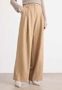 Beige wijde broek met plooien, gemaakt van een gestructureerde stof, gecombineerd met lichtgrijze puntige hakken. Minimalistisch ontwerp met strakke lijnen.