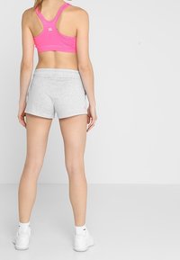 Růžová sportovní podprsenka, šedé šortky. Podprsenka má závodní střih na zádech; šortky jsou ze měkké látky s elastickým pasem. Bílé tenisky s doplňky.