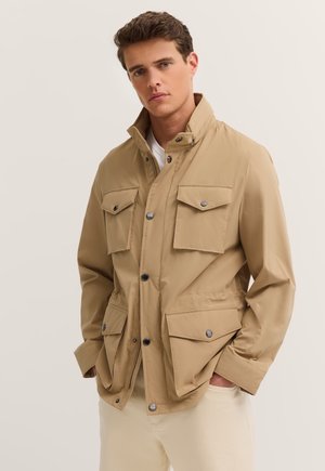 Beige, leichte Jacke mit hohem Kragen, Druckknöpfen und mehreren Vordertaschen. Glatte Textur mit entspannter Passform.