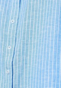 Camicia azzurro chiaro con righe verticali bianche. Realizzata in tessuto texturizzato, presenta bottoni bianchi rotondi lungo la parte anteriore.