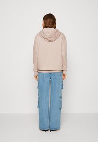 Felpa leggera beige con cappuccio regolabile, abbinata a pantaloni cargo in denim azzurro a gamba larga, dotati di tasche laterali e bordi sfrangiati.