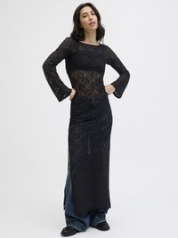 Vestido de renda preta com mangas longas e punhos amplos, apresentando uma sobreposição transparente e um design em camadas. Combinado com jeans de perna larga.