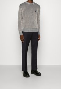 Gestreifter Strickpullover in grau und weiß mit gerippten Bündchen, kombiniert mit einer navyblauen Hose und schwarzen Schnürschuhen. Texturierte Stoffdetails sichtbar.