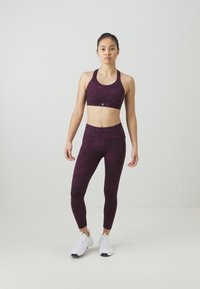 Športni modrček in legice v temno vijolični barvi z diskretnim vzorcem živali. Narejeno iz elastičnega materiala, v kompletu z belimi športnimi čevlji.