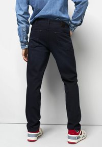 Marineblaue Jeans mit einer taillierten Passform, Gesäßtaschen mit gestickten Akzenten, kombiniert mit roten und weißen Sneakers.