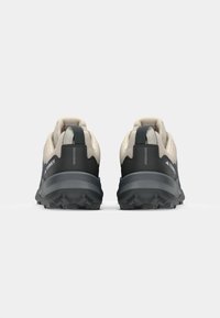 Zapatillas de trail running con parte superior beige y suela negra. Cuentan con una suela texturizada, cuello acolchado y talón reforzado.