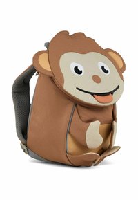 Mochila en forma de mono marrón con correas grises, que presenta una cara caricaturesca, orejas y una superficie de tela texturizada. Incluye un bolsillo con cremallera en la parte frontal.