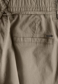 Beige kankaita sihikhururu dzinoratidza chirevo chakatwasuka, elastic waistband, uye kibhu kumashure ine chichena chemetali. Mvura inofukidza cotton yakanakisa.