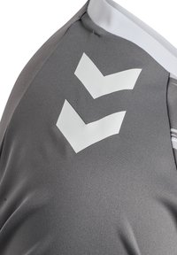 Grå sportskjorta med strukturerat tyg. Har en vit rund hals och en framträdande vit chevronlogotyp på vänster axel.