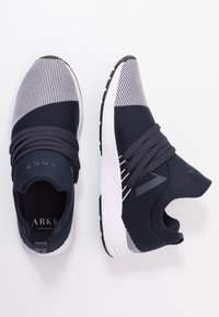 Granatowe i szare buty sportowe z siateczkową cholewką, elastycznymi sznurówkami i białą podeszwą środkową; zaokrąglony czubek i teksturowana gumowa podeszwa.