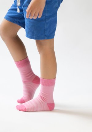 Rosa gestreifte Socken mit einer einfarbigen pinken Spitze und einem gerippten Bündchen, getragen mit blauen Shorts, die eine weiche Textur und lebendige Farben zeigen.