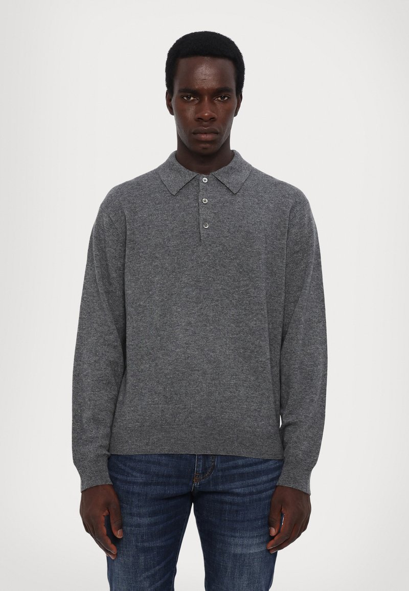 Grauer Pullover mit kragen und drei Knöpfen, aus einem strukturierten Strickstoff. Lange Ärmel, Saum auf Hüfthöhe, kombiniert mit blauen Jeans.