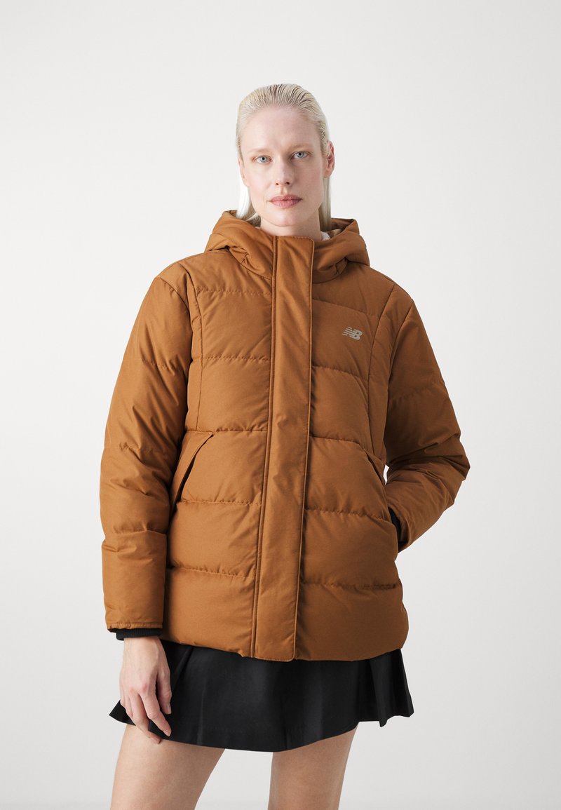 Veste matelassée marron avec capuche, dotée d'une fermeture éclair verticale à l'avant, de poches latérales et d'un logo discret sur la poitrine. Texture lisse.