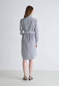Stripet skjortekjole i blått og hvitt, med lange ermer, belte i midjen og knelengde. Glatt stoff med en skreddersydd silhuett.