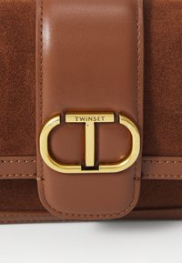 Borsa in pelle e suede marrone con un clasp a logo in oro e dettagli di cucitura. Forma strutturata con una superficie liscia.