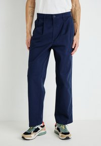 Navy blue, pleated pants made of cotton; features a fitted waist with a button closure and side pockets for utility.