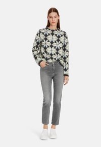 Gebreide trui met een multicolor geometrisch patroon, grijze jeans en witte instapschoenen. Zachte textuur, relaxte pasvorm, ronde halslijn.