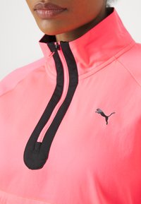 Veste fuchsia à ZIP quarts avec accents noirs, présentant un design élégant et un logo Puma sur la poitrine. Tissu doux et col haut.