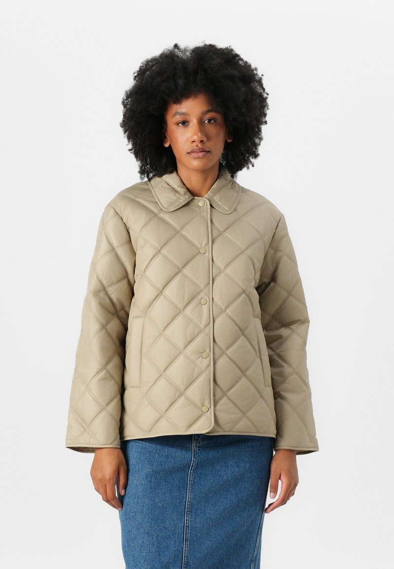 Veste matelassée beige avec un col, fermeture à boutons à l'avant et manches longues, associée à une jupe en denim. Texture lisse.