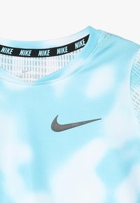 Camiseta deportiva Nike en azul claro con un patrón de tie-dye. Presenta una banda negra con la marca "NIKE" y un logotipo gris en la parte delantera.