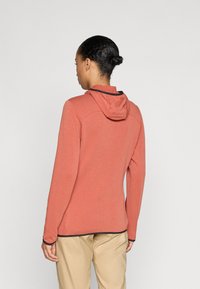 Φόρμα με κουκούλα σε ξεθωριασμένο κοραλί, φτιαγμένη από μαλακό, υφασμάτινο υλικό. Διαθέτει μαύρες λεπτομέρειες στην κουκούλα και στα μανίκια, με άνετη εφαρμογή.