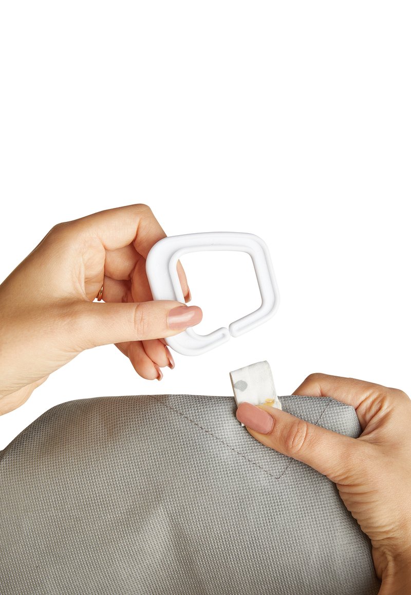 White plastic clip held above a light gray textured fabric, with a looped tag visible on the corner. Hand shows grip on both items.