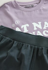 Ljuslila bomullströja med vit text, matchad med mörkgröna shorts med elastisk midja gjorda av mjukt tyg, som visar en samlad textur.