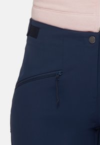 Granatowe spodnie sportowe o teksturowanym wykończeniu, z zamkiem błyskawicznym w kieszeni, sznurkiem do regulacji oraz akcentem na rzep na pasie.