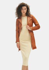 Tan leather jacket with lapel collar and button closures, paired with a fitted cream-colored dress. Smooth texture, mid-length design.