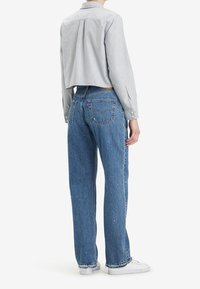 Camisa de rayas corta con mangas largas combinada con jeans de tiro alto azules. Los jeans tienen un acabado desgastado y un diseño clásico de dos bolsillos.