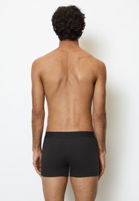 Boxer briefs neri in cotone con una texture liscia e una cintura elastica, mostrati da dietro su un torso nudo contro uno sfondo bianco.