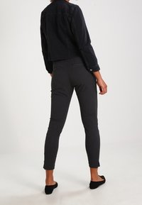 Svart cropped denimjacka med långa ärmar, kombinerad med åtsittande mörkgrå byxor som har en texturerad tygkvalitet och sprund vid vristerna.