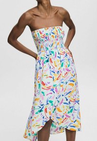 Abito midi bianco senza spalline con motivi astratti colorati a pennellate, corpetto arricciato e gonna in stile incrociato indossato da una modella di carnagione scura.